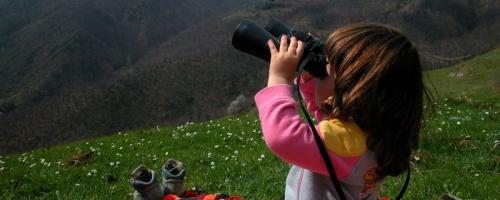 Bambina che scruta con un binocolo il paesaggio